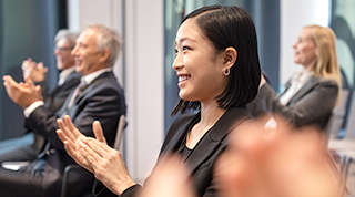 Une dirigeante asiatique applaudit, assise dans une salle avec ses collègues à une conférence.