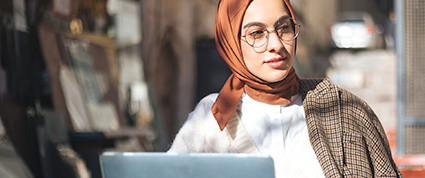 Une femme portant un hijab travaille sur un ordinateur portable, assise dehors un jour d’automne.